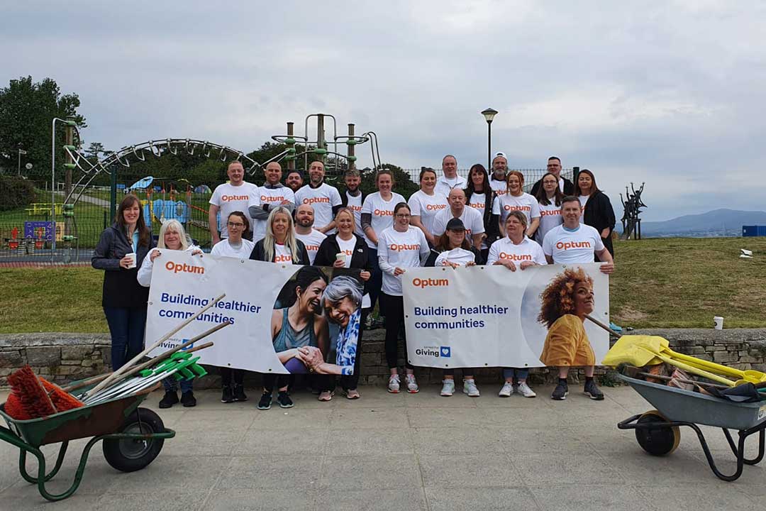 A large group of Optum colleagues in front of a community playground holding Optum Giving banners 