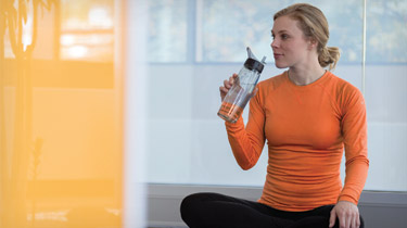Woman in workout clothes sitting on the floor drinking water from a water bottle