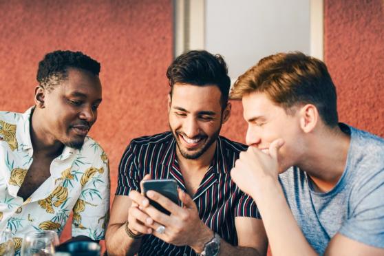 Three young adult men looking at a phone